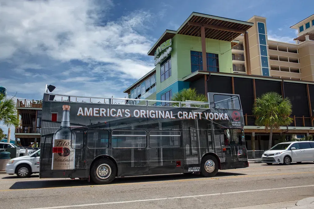 A bus is parked in front of a building that says america 's original craft vodka.