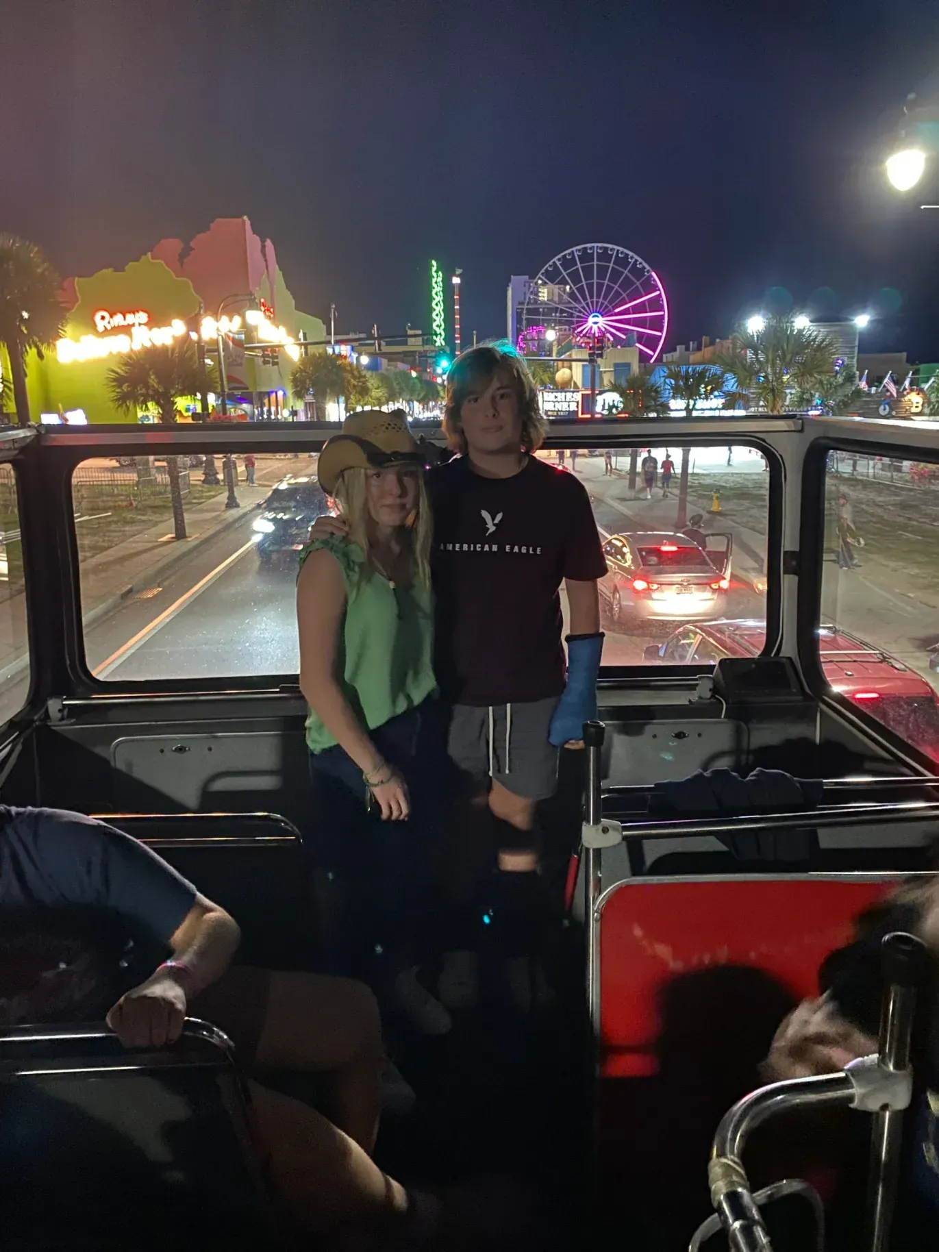 A man and a woman are standing in the back of a bus at night.