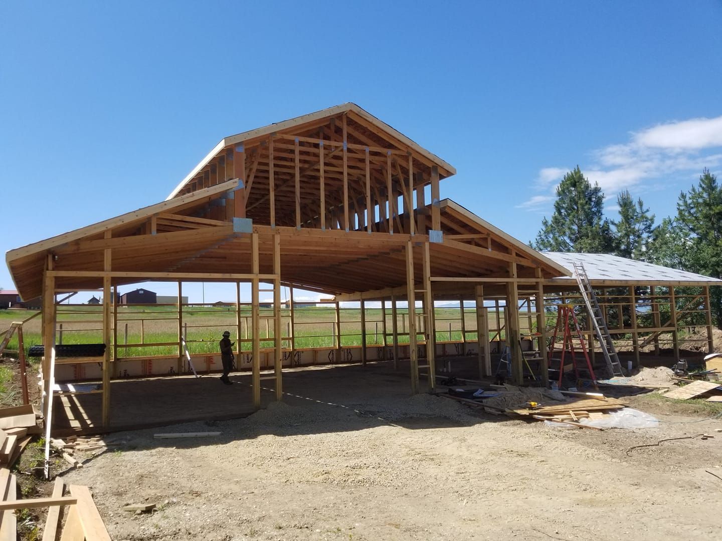 A large wooden barn is being built in a dirt field.
