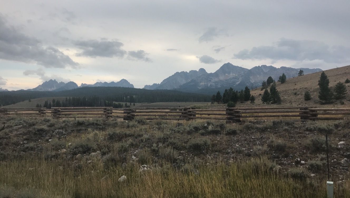 A wooden fence surrounds a grassy field with mountains in the background.