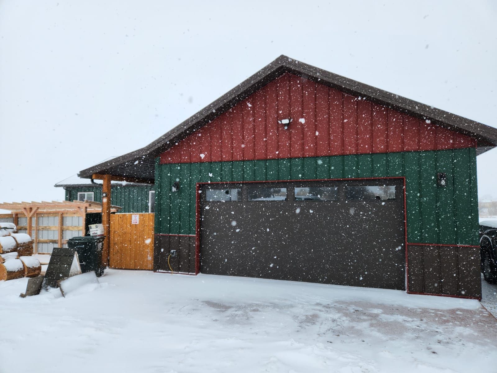 A garage with a red and green roof is covered in snow.