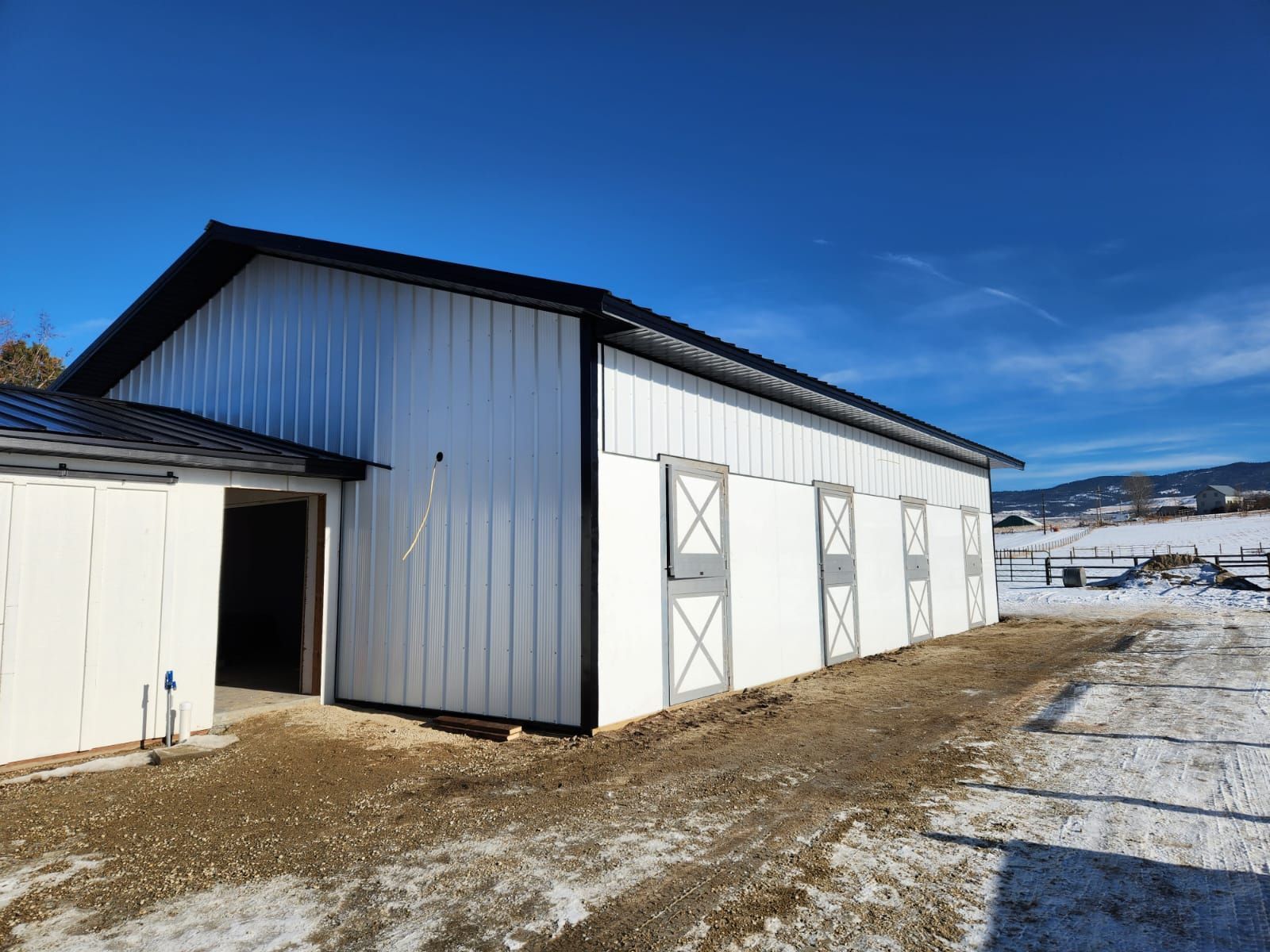 A white barn with a black roof is sitting in the snow.