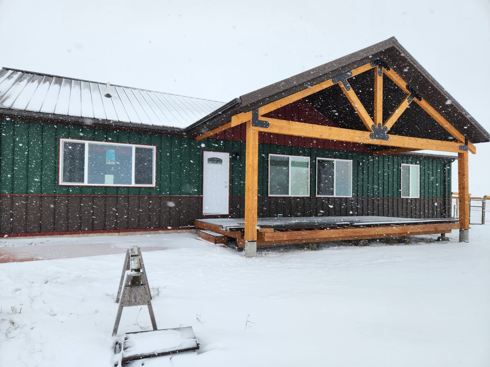 A green house with a porch in the snow.