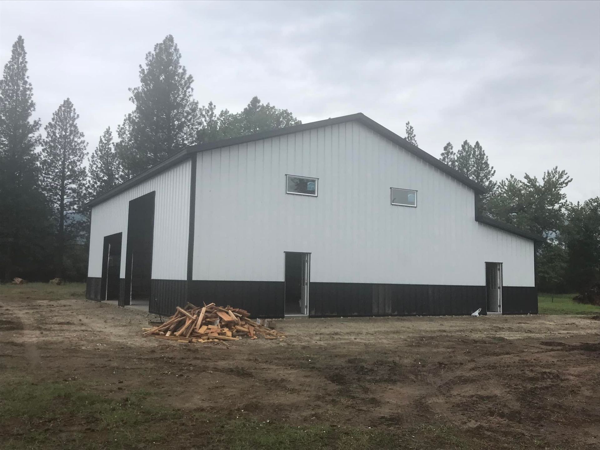A white and black building with a pile of wood in front of it