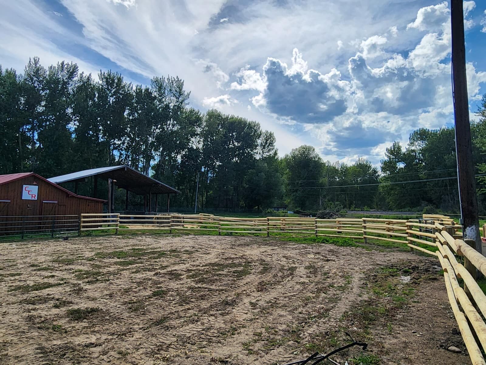 A wooden fence surrounds a dirt field with trees in the background.
