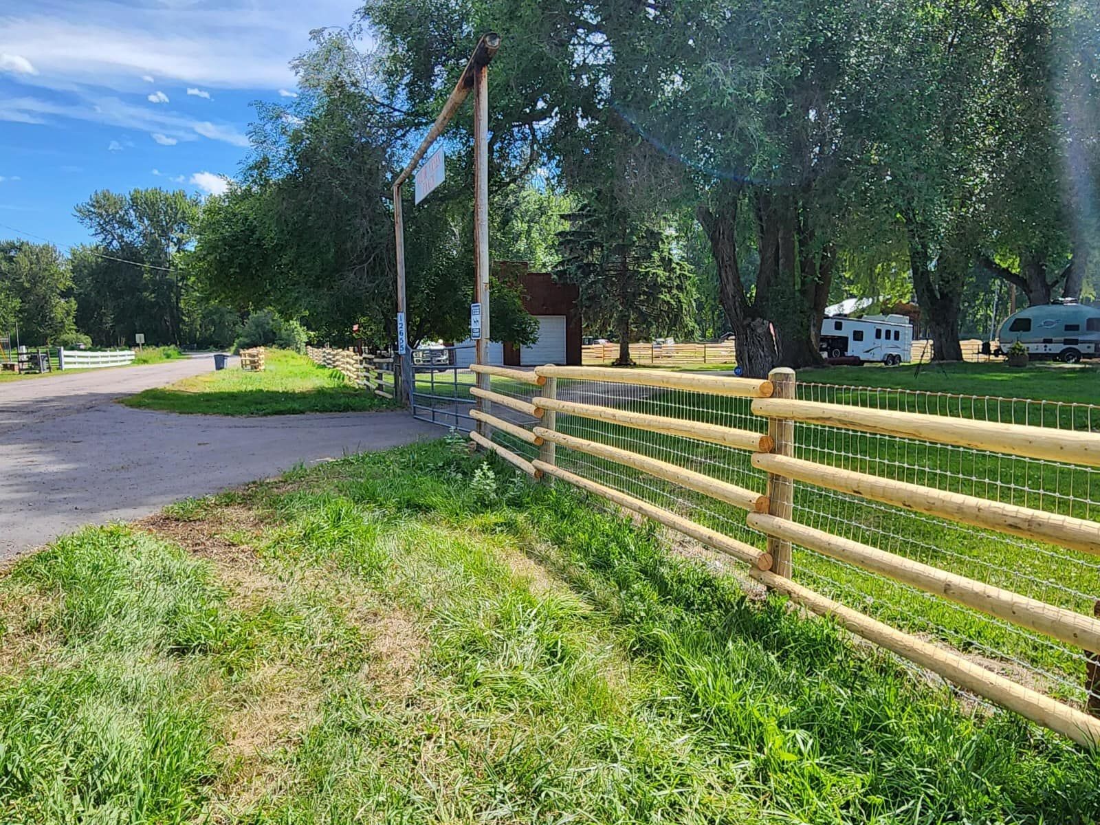 A wooden fence surrounds a grassy field next to a road.