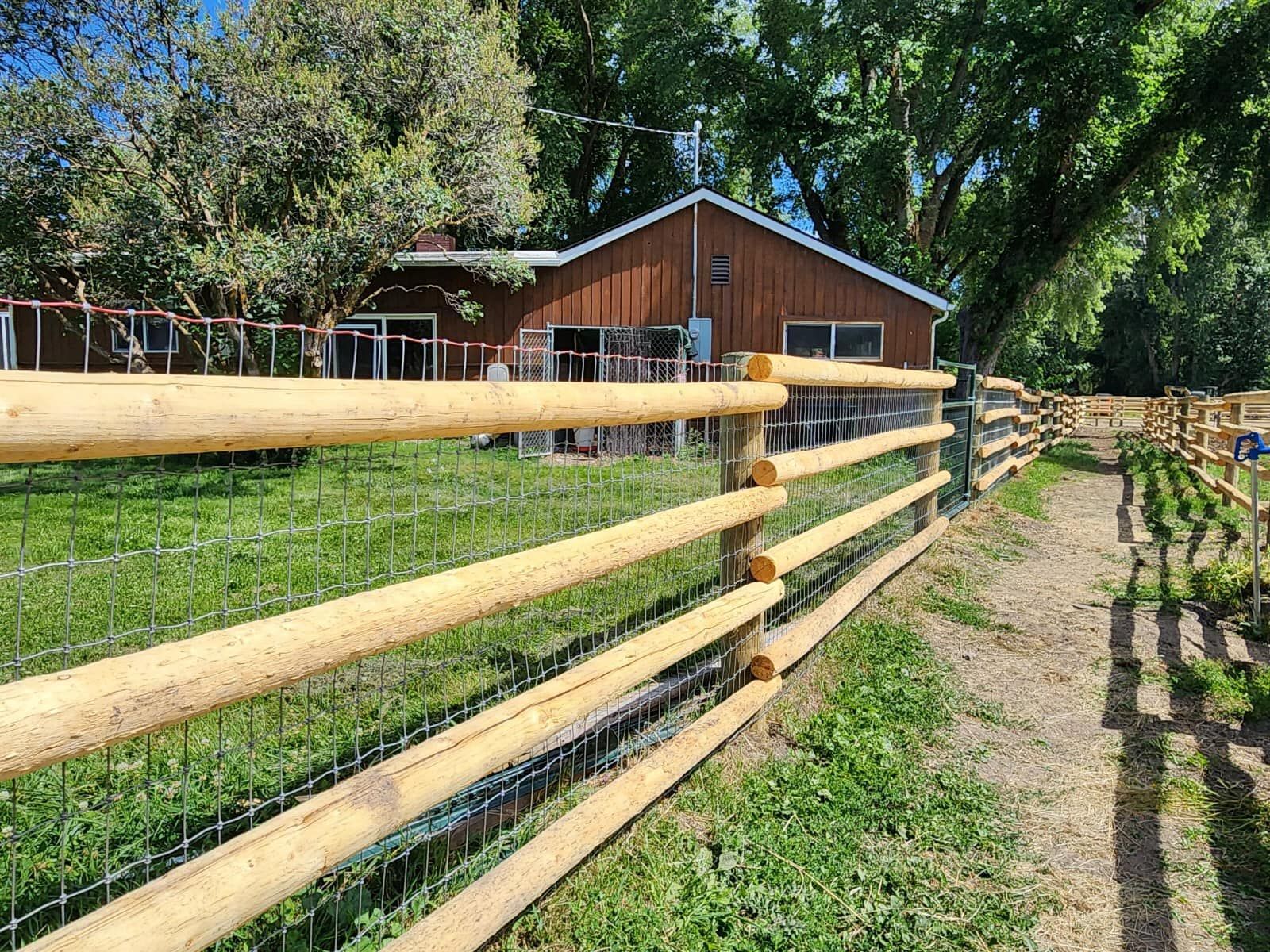 A wooden fence surrounds a grassy field in front of a barn.