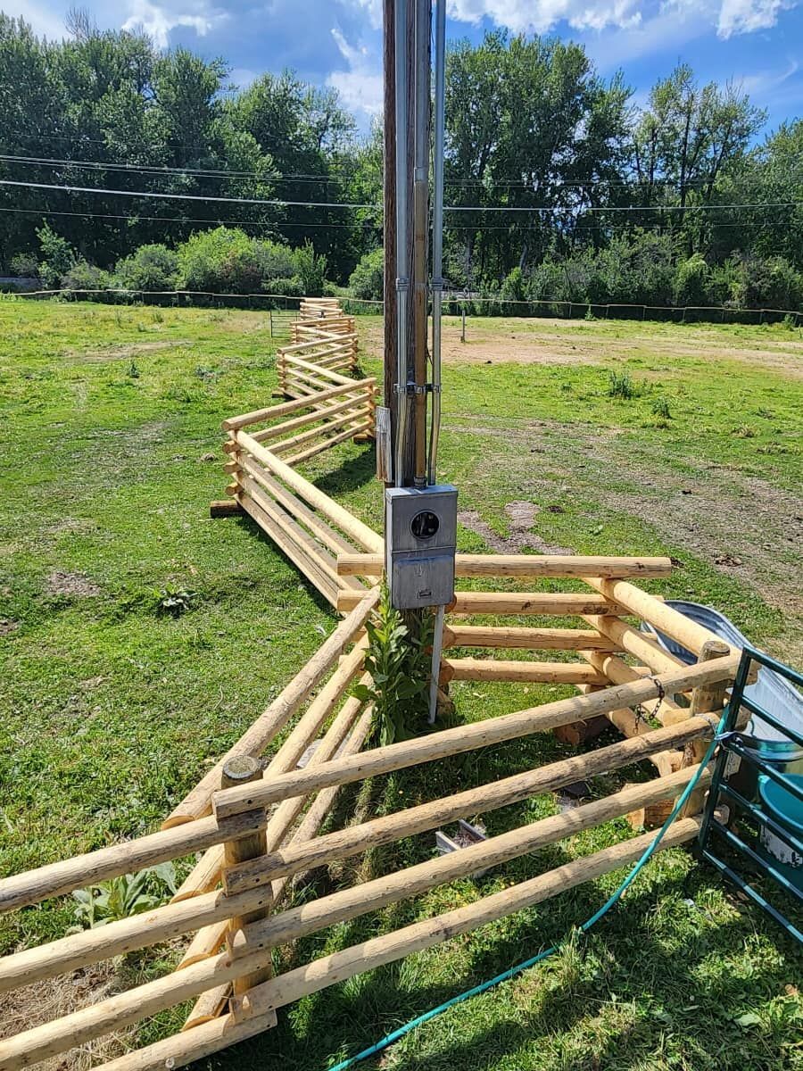A wooden fence is surrounding a pole in a field.