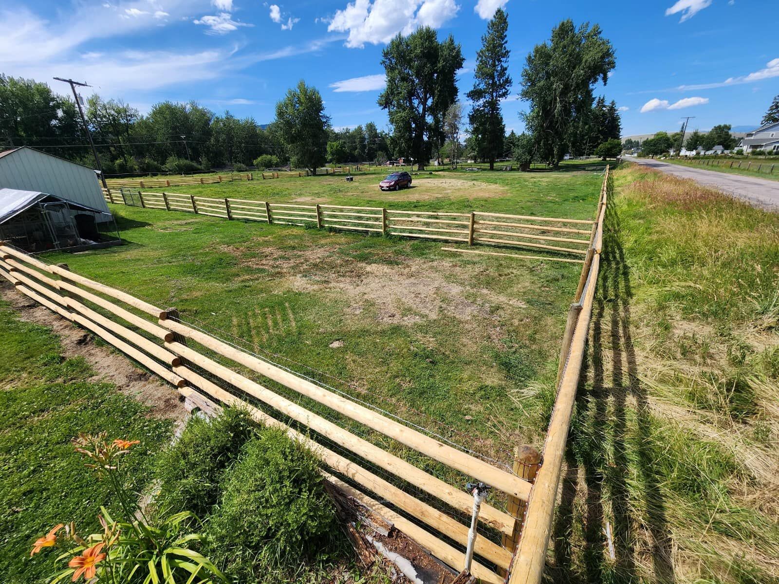 A wooden fence surrounds a grassy field next to a road.