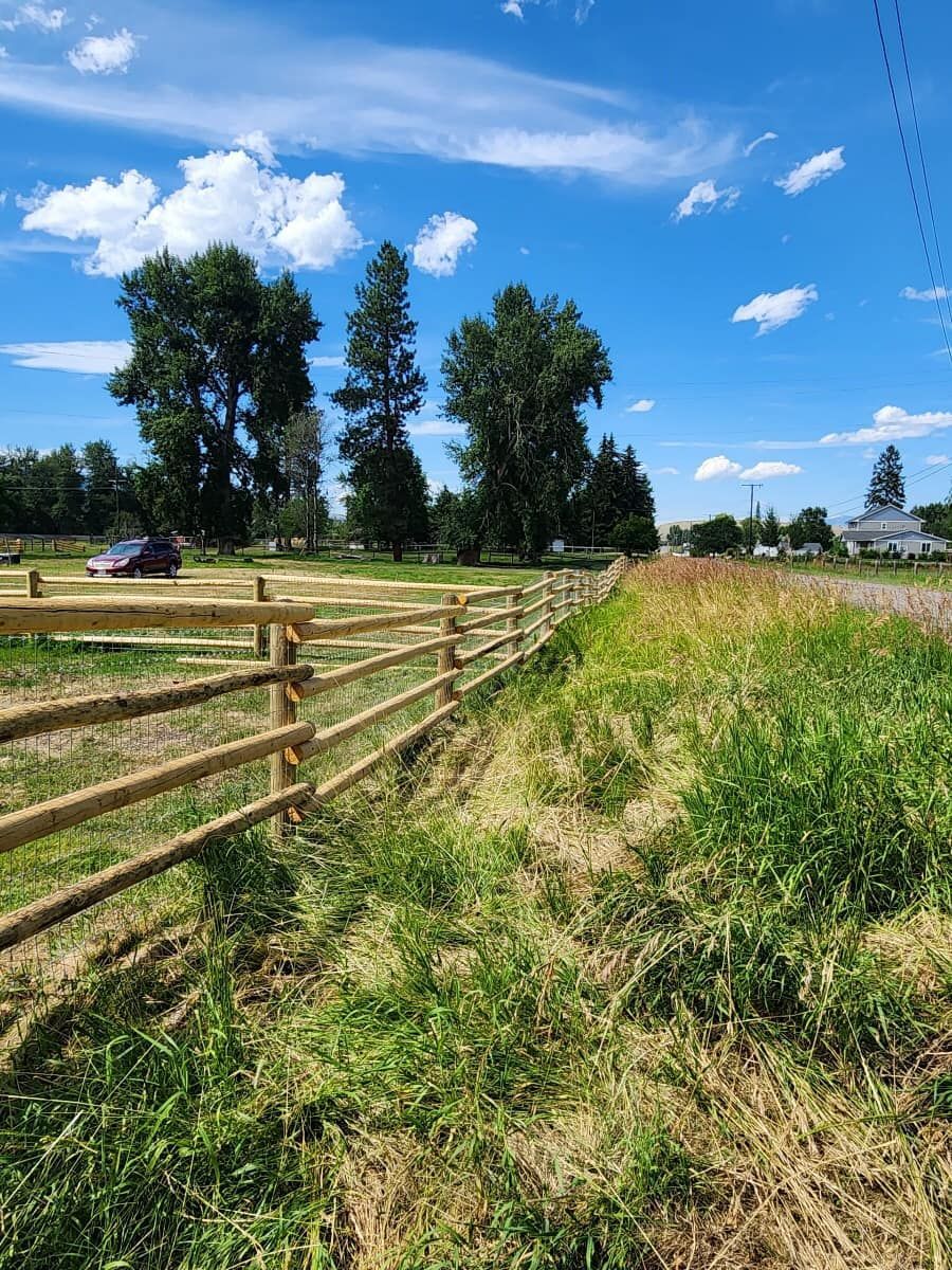A wooden fence surrounds a grassy field on a sunny day.