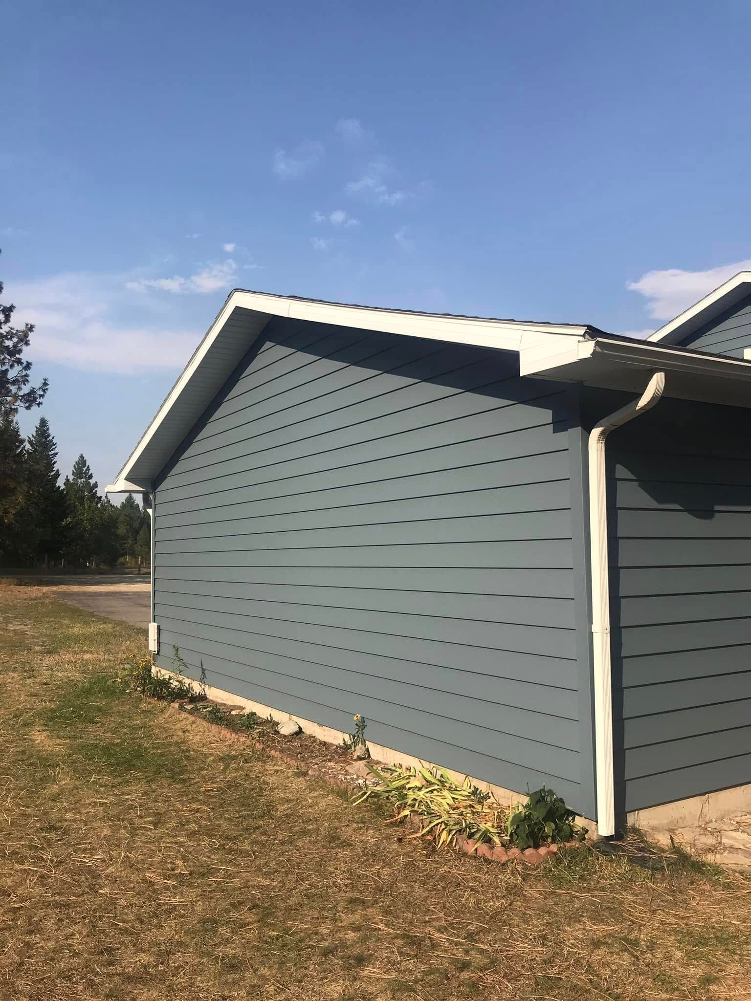 A blue house with a white roof is sitting in the middle of a grassy field.