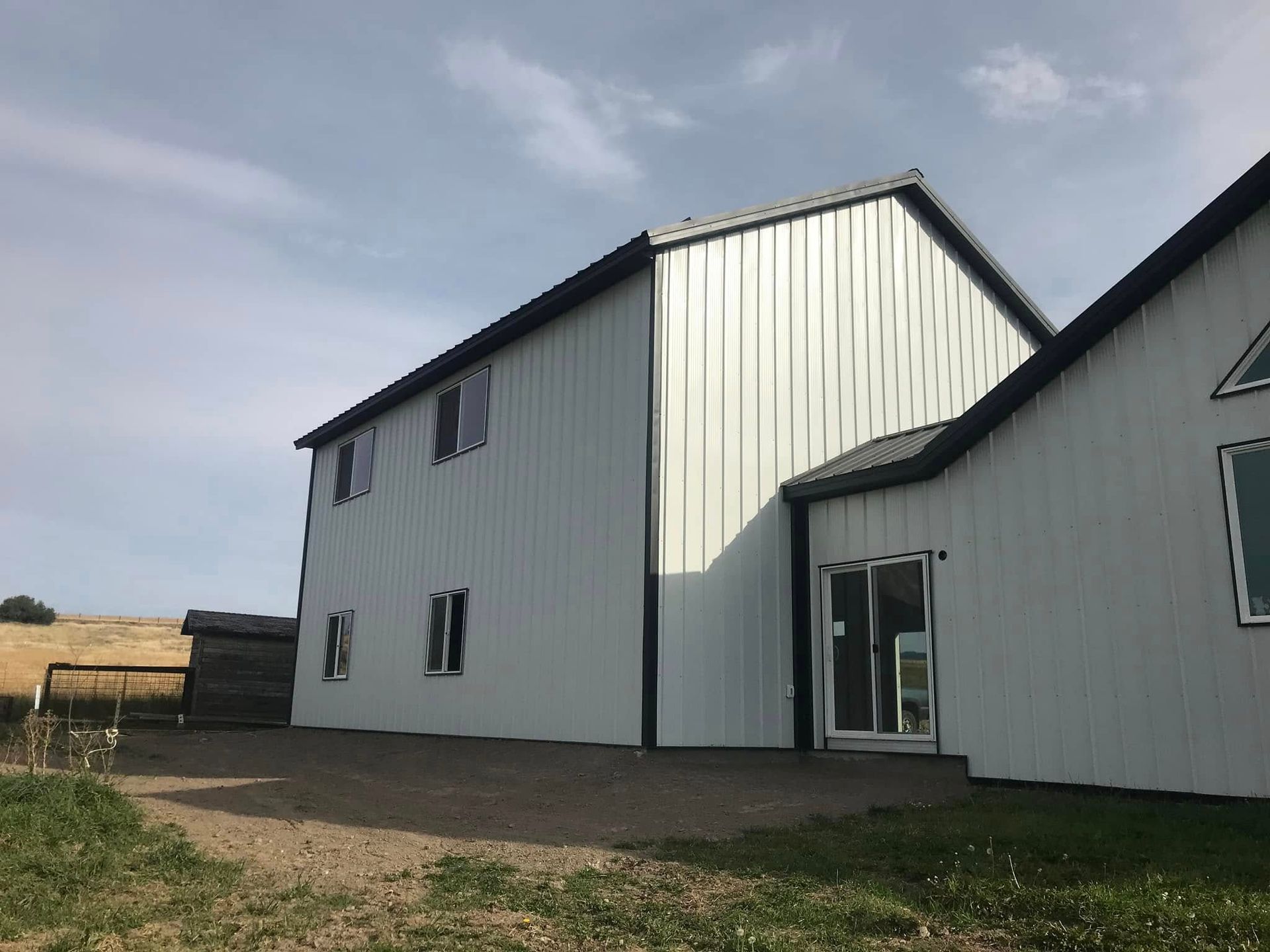 A large white building with a black roof is sitting in the middle of a grassy field.