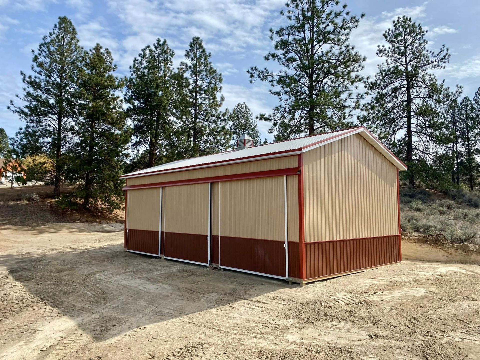 A large metal building with a red trim is sitting in the middle of a dirt field.