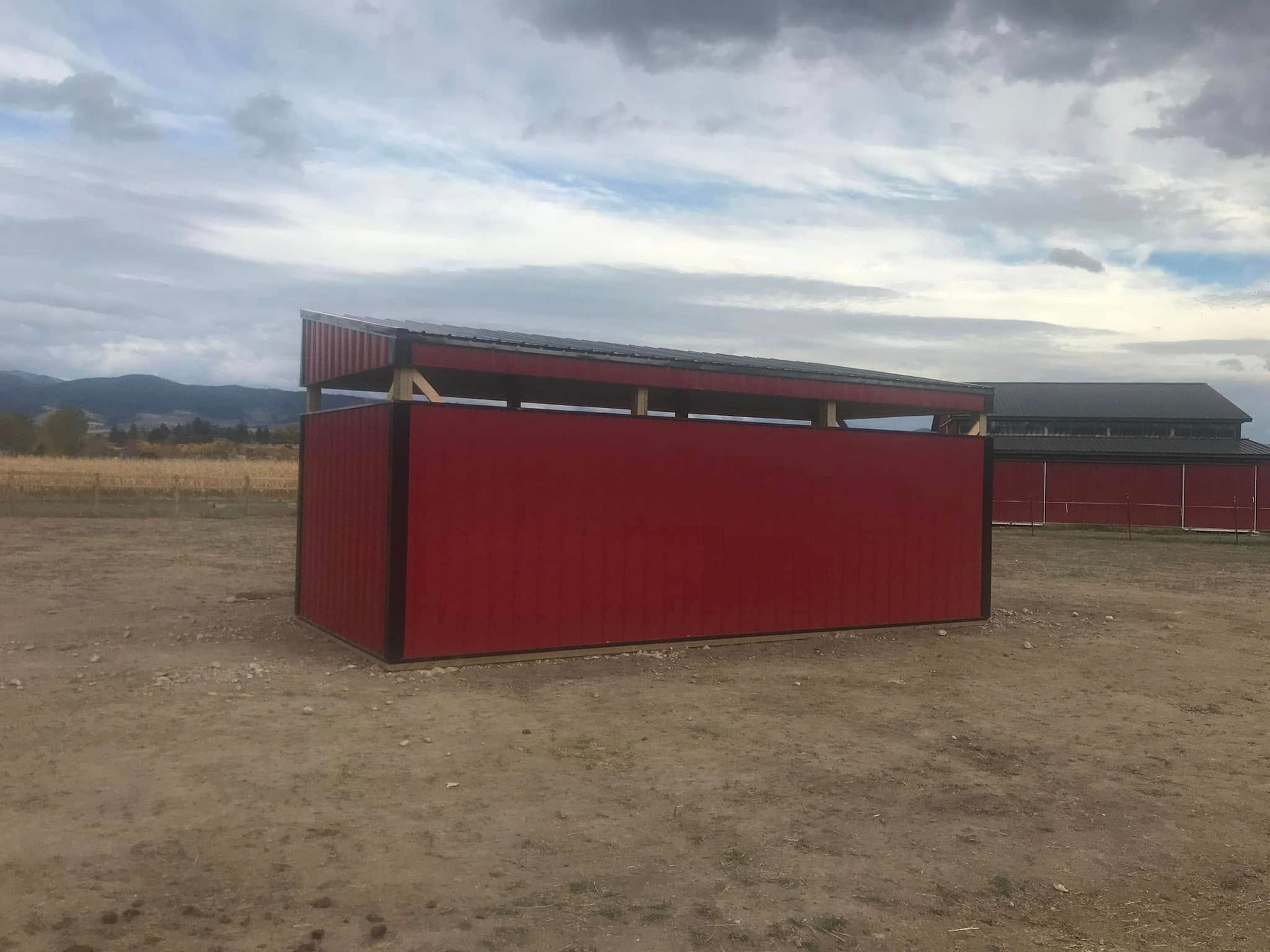 A red building is sitting in the middle of a dirt field.