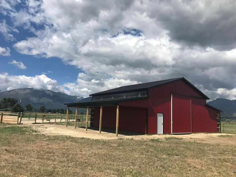 A red barn is sitting in the middle of a field with mountains in the background.