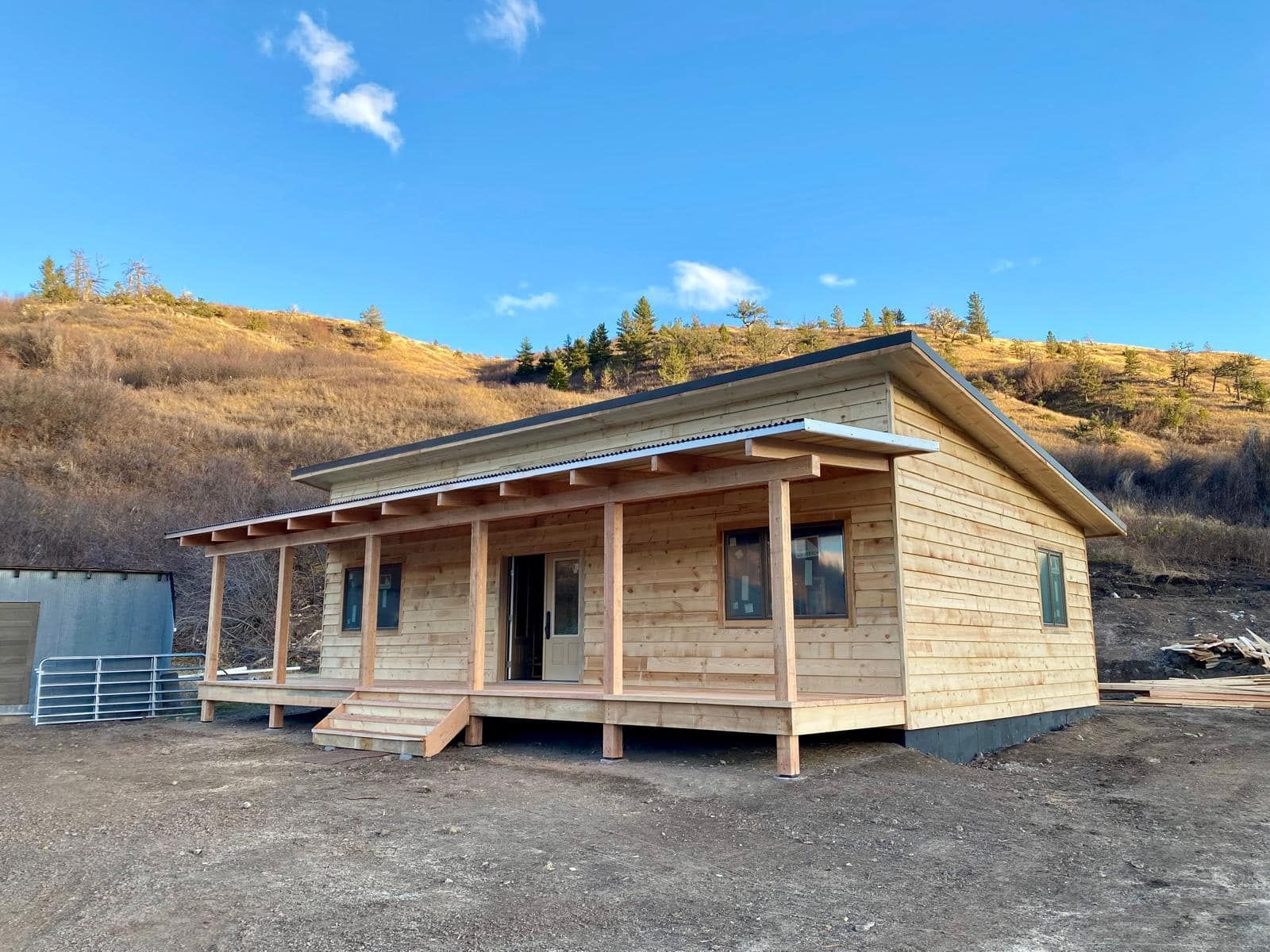 A small wooden house with a porch in the middle of a dirt field.