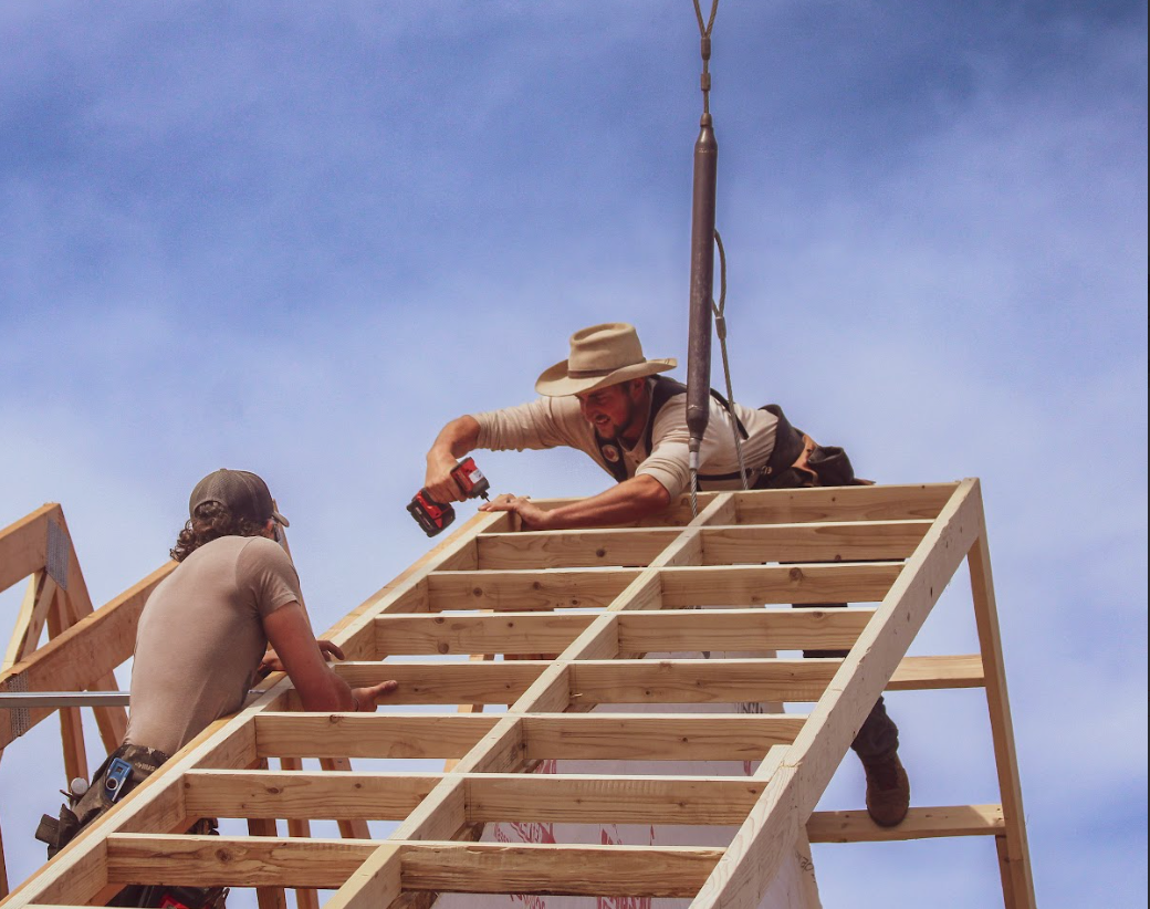 A large metal building with a red trim is sitting in the middle of a dirt field.