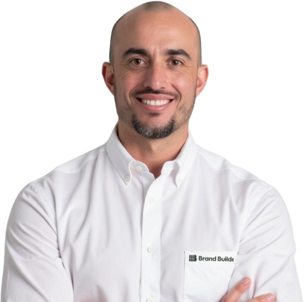 A bald man with a beard wearing a white shirt that says grand builds