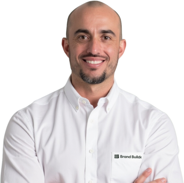 A bald man with a beard wearing a white shirt that says grand builds