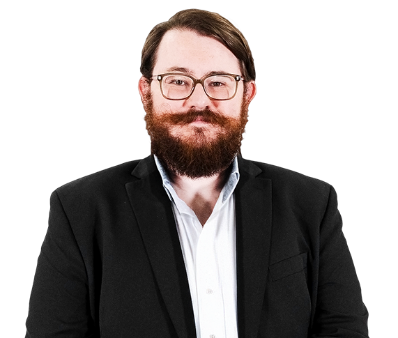 Smiling person with glasses and beard wearing a black blazer over a white shirt on a white background