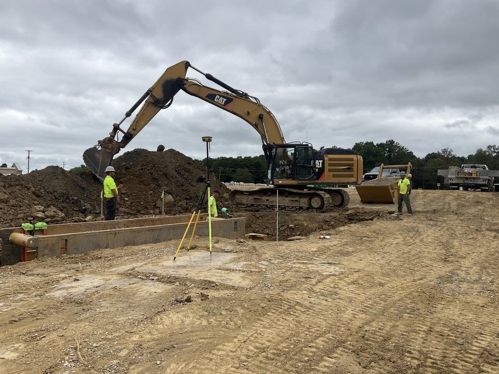 Excavator loading dirt at a muddy construction site with workers in neon safety vests