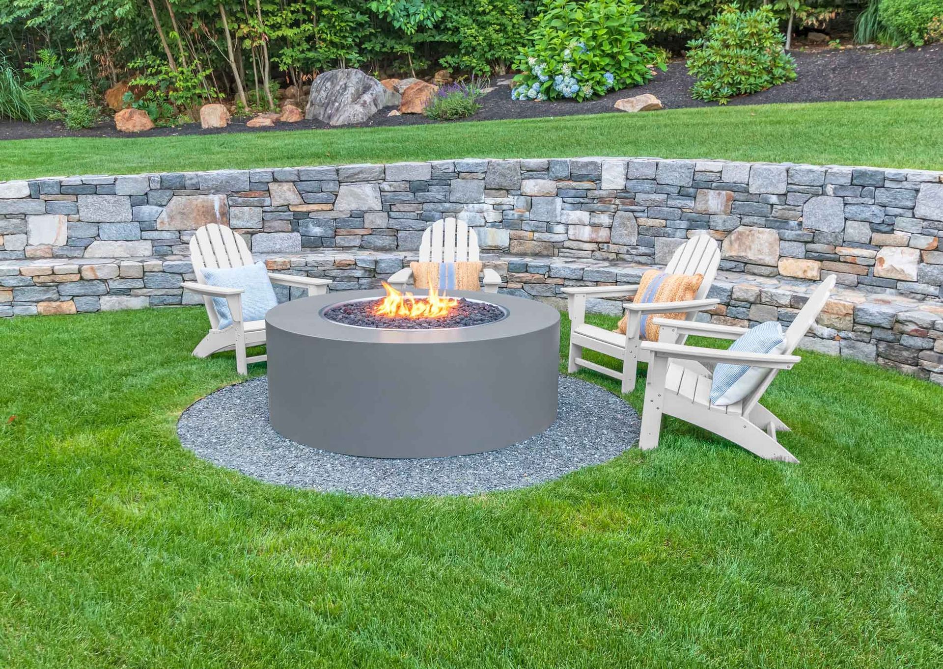 There is a fire pit in the middle of the lawn surrounded by chairs.