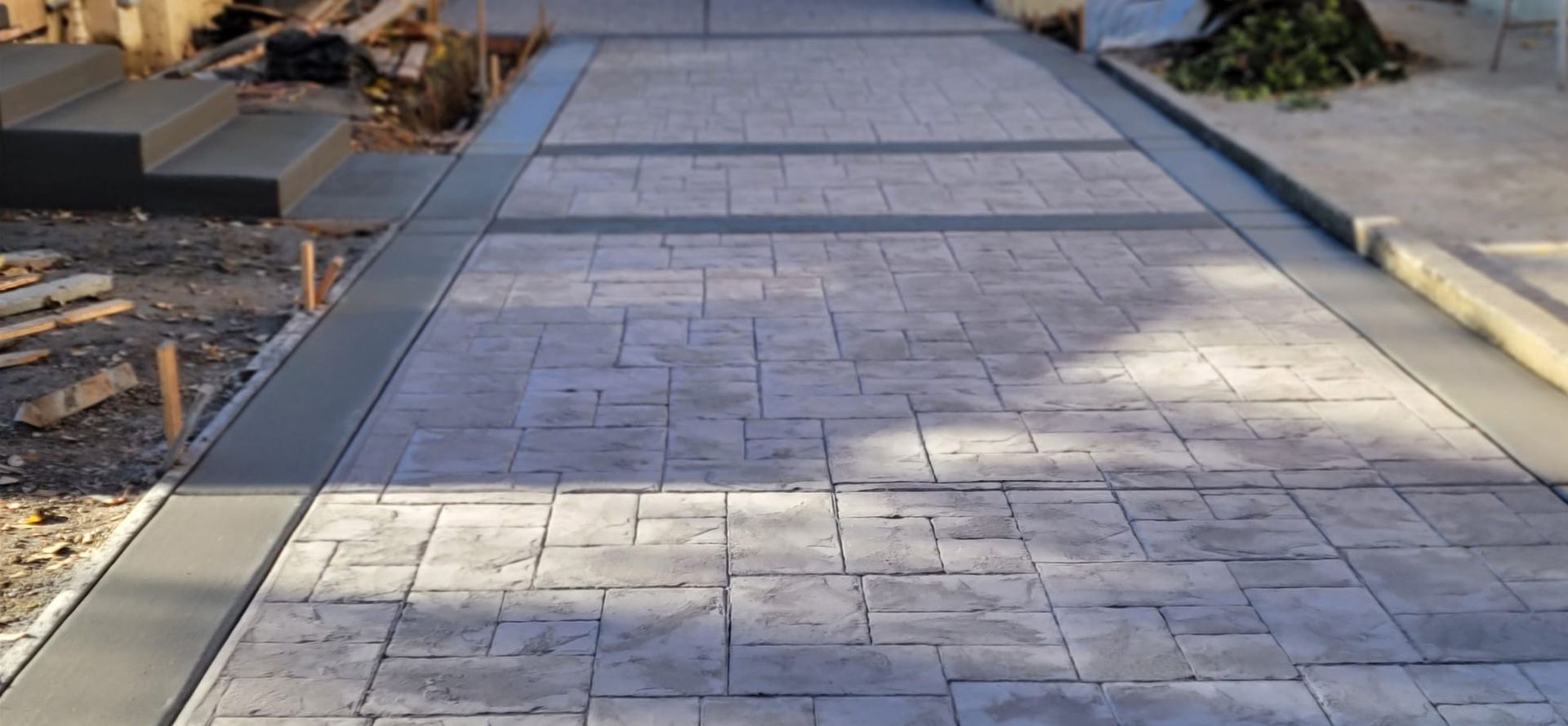 A concrete walkway with a tree stump in the background is being built.