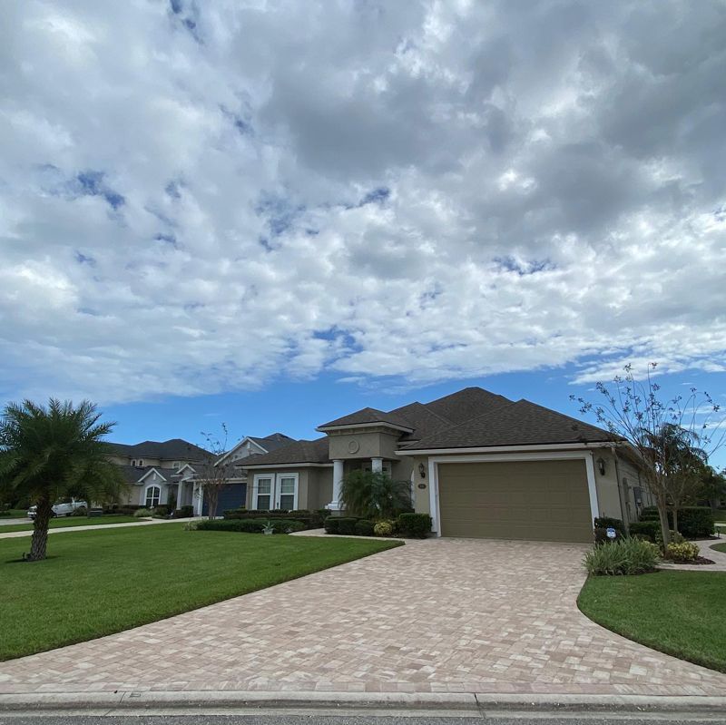 A large house with a brick driveway and a palm tree in front of it.