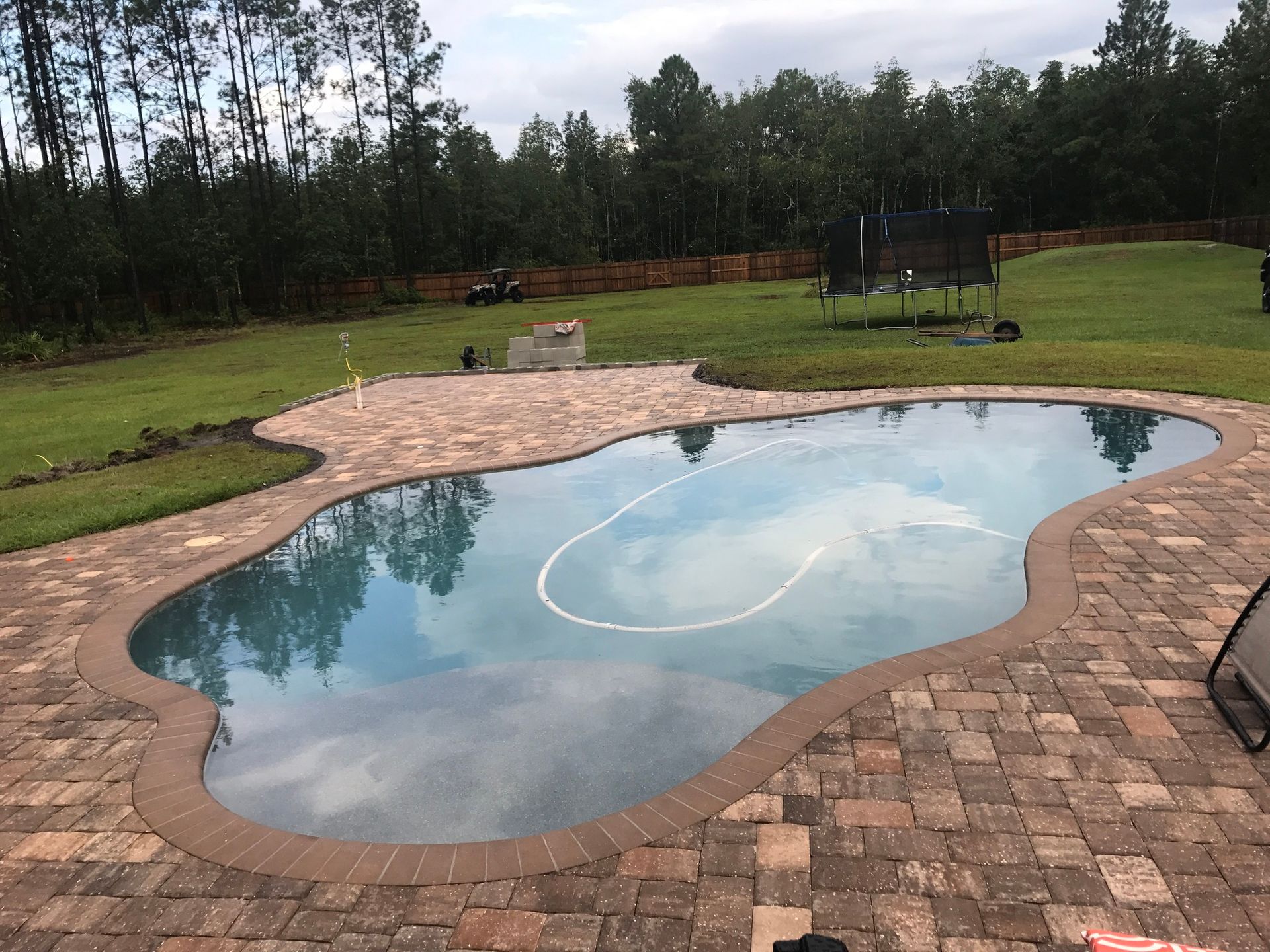 A large swimming pool with a brick pavement in the background