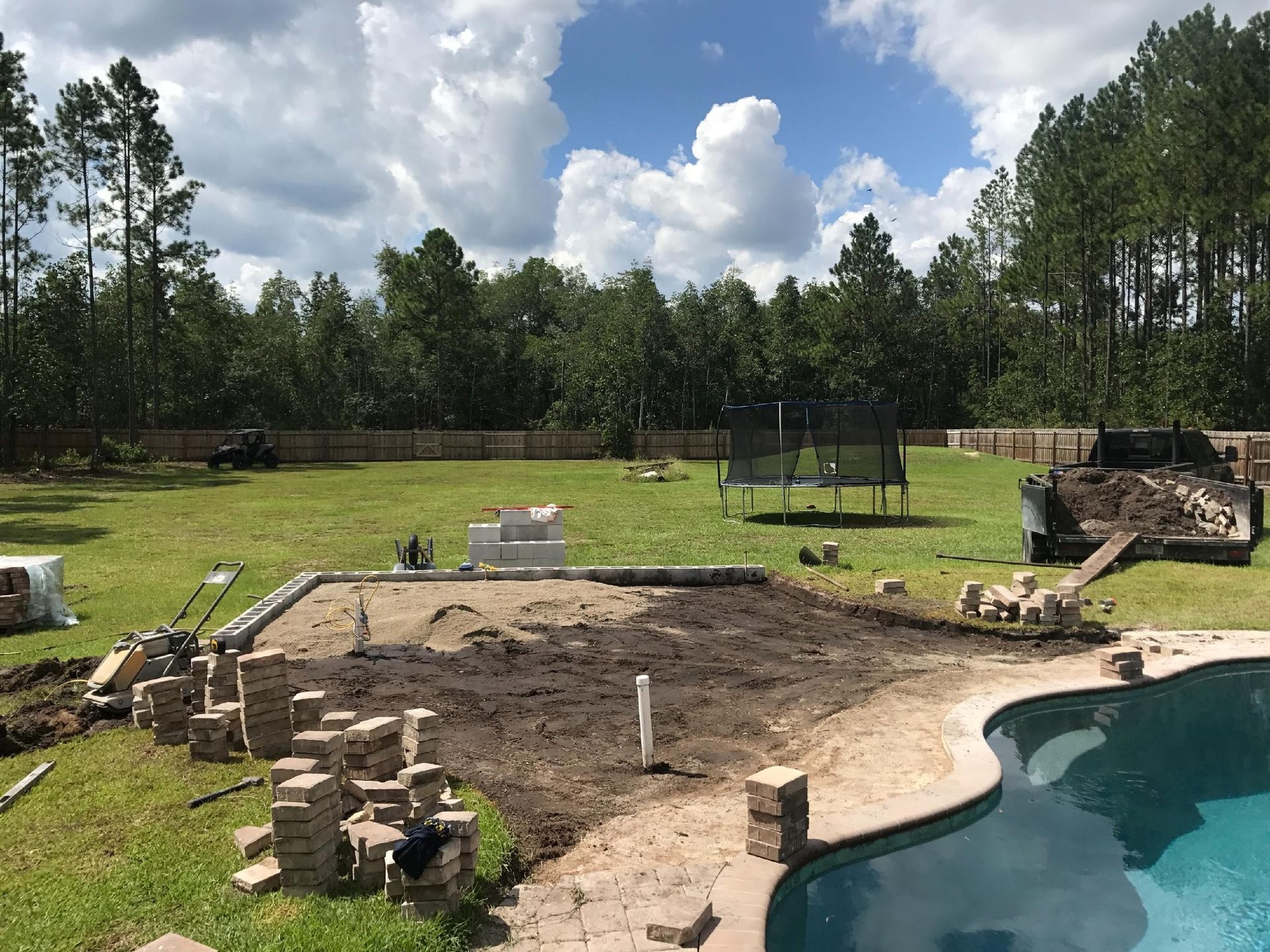 A swimming pool patio is being built in the backyard of a house.