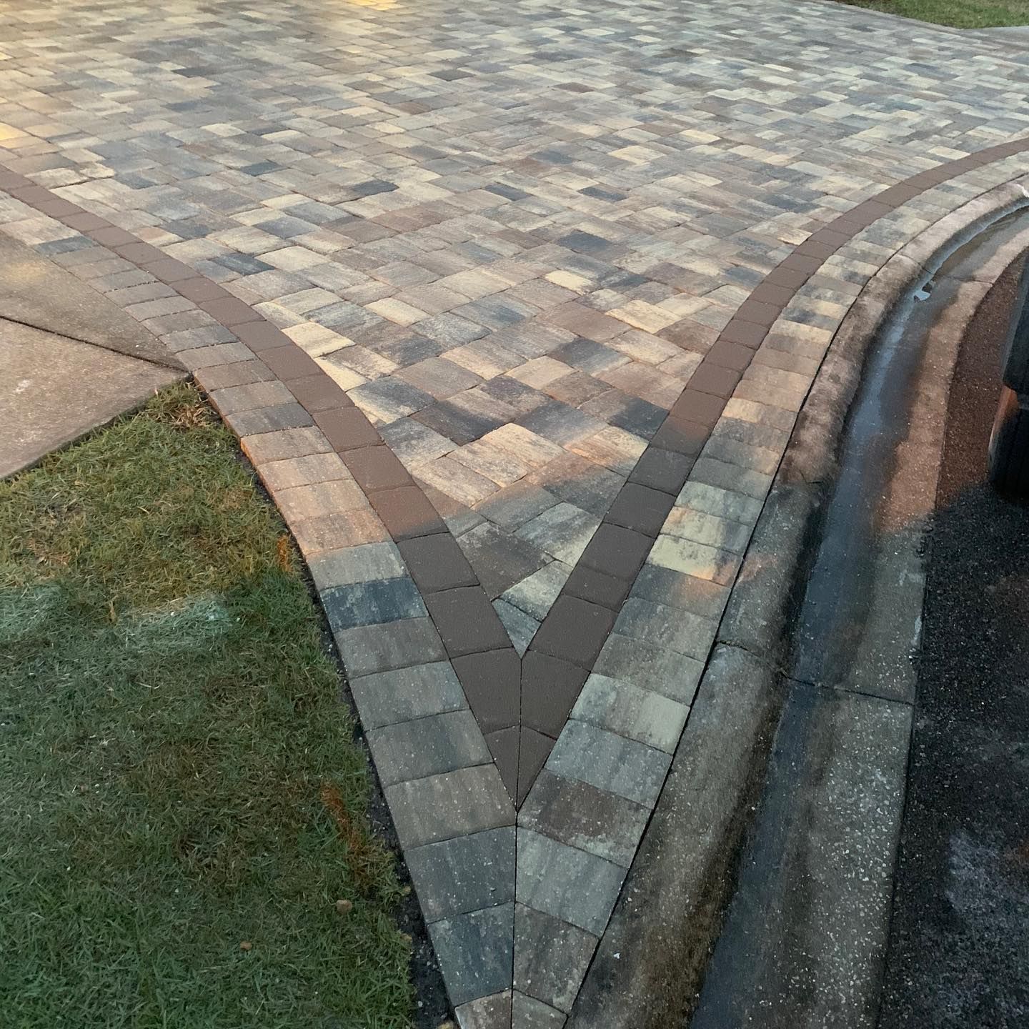 A brick driveway with a curb and grass on the side of it.