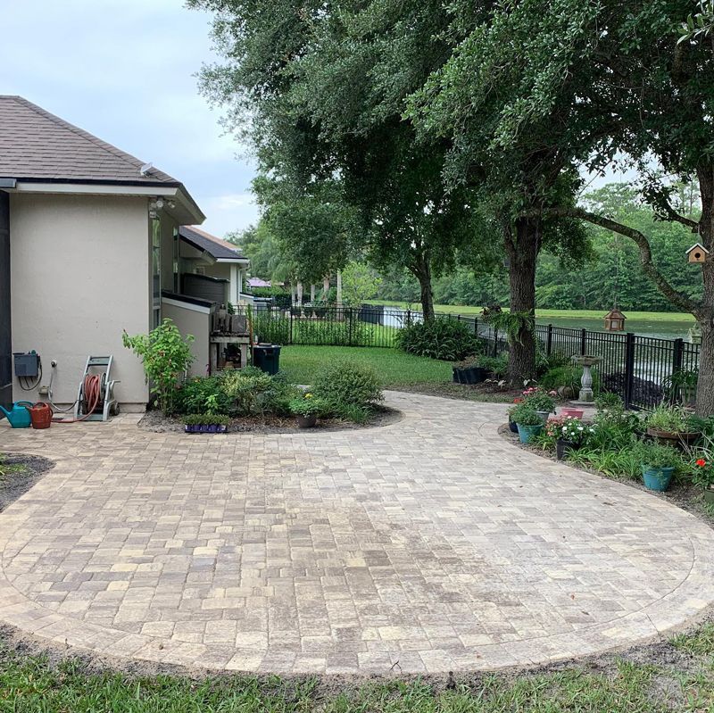 A brick driveway leading to a house with a pond in the background.