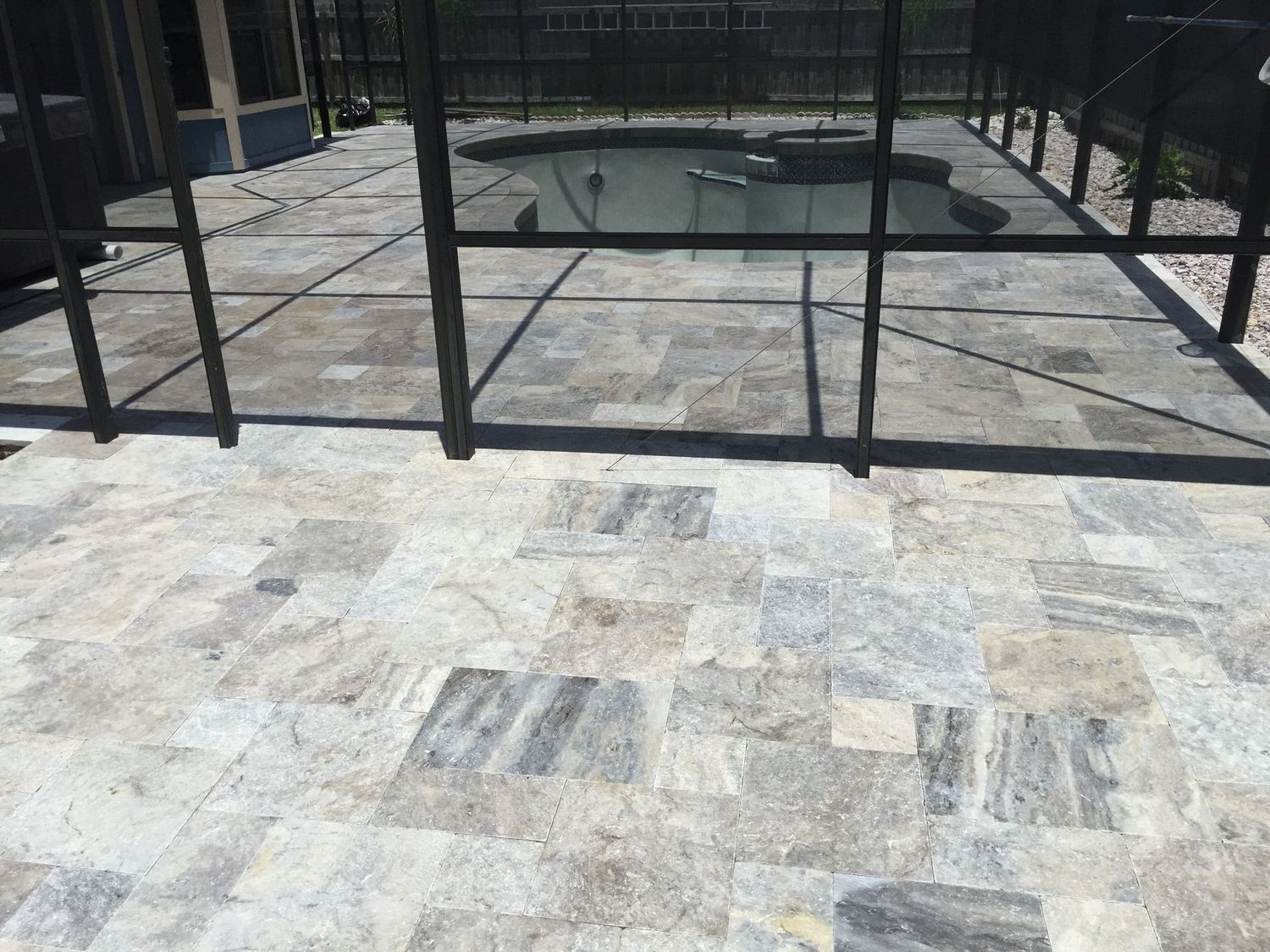 A screened in patio with a pool in the background.