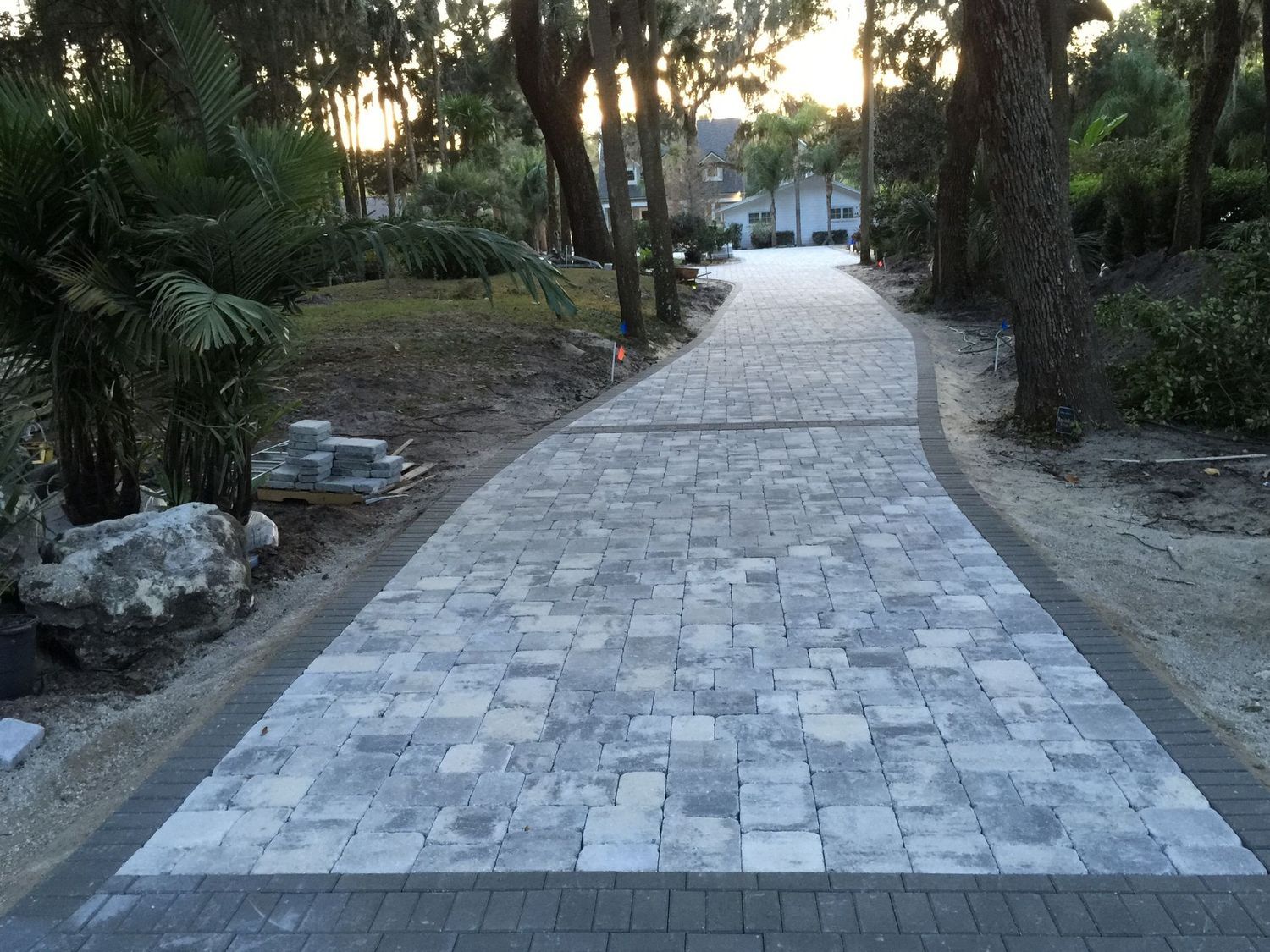 A brick driveway leading to a house surrounded by trees