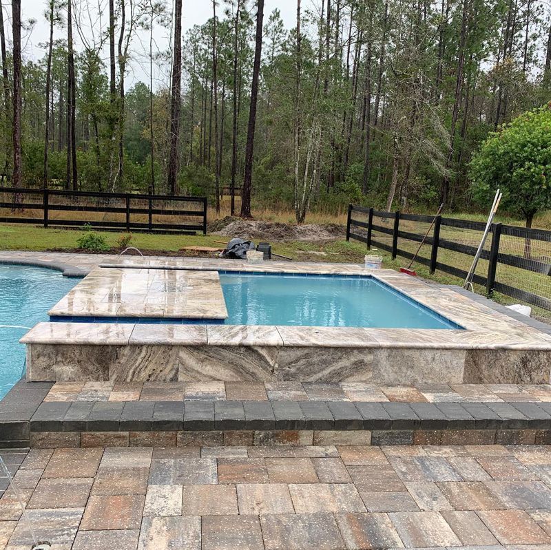 A large swimming pool with a fence in the background stone pavement.