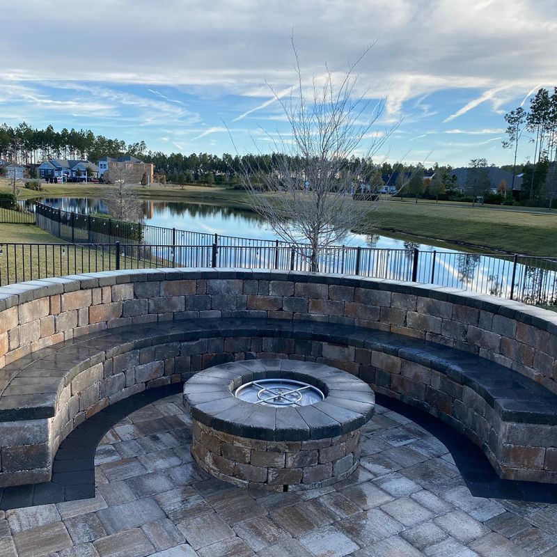 A fire pit in the middle of a brick patio with a lake in the background