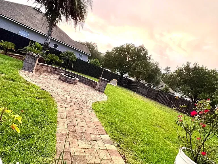 A brick walkway leading to a fire pit in a backyard.
