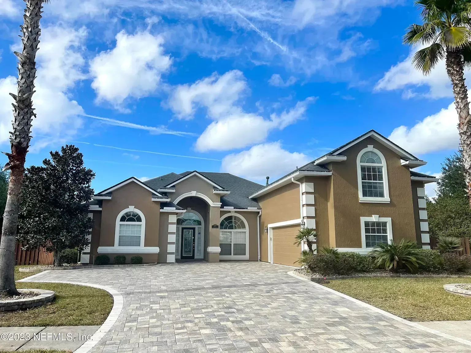 A large house with a brick driveway and palm trees in front of it