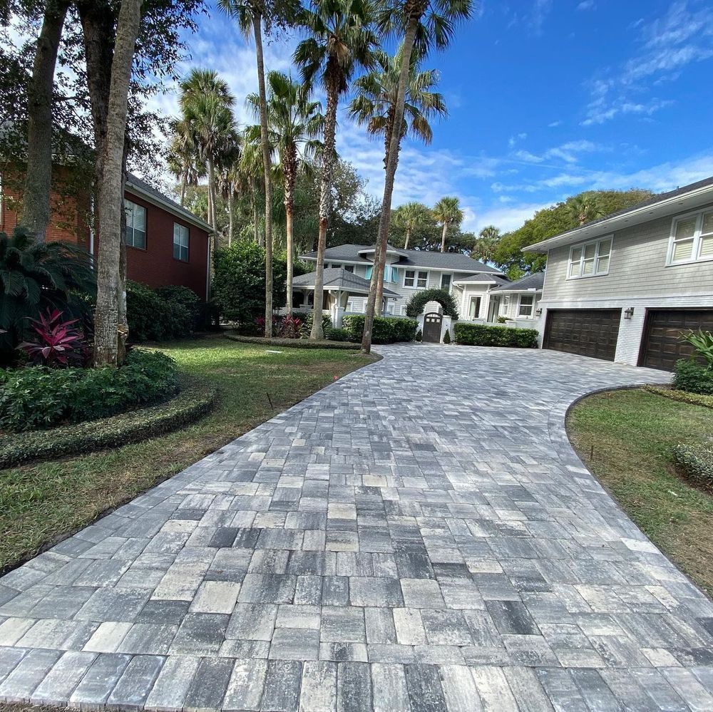 A brick driveway leading to a house with palm trees