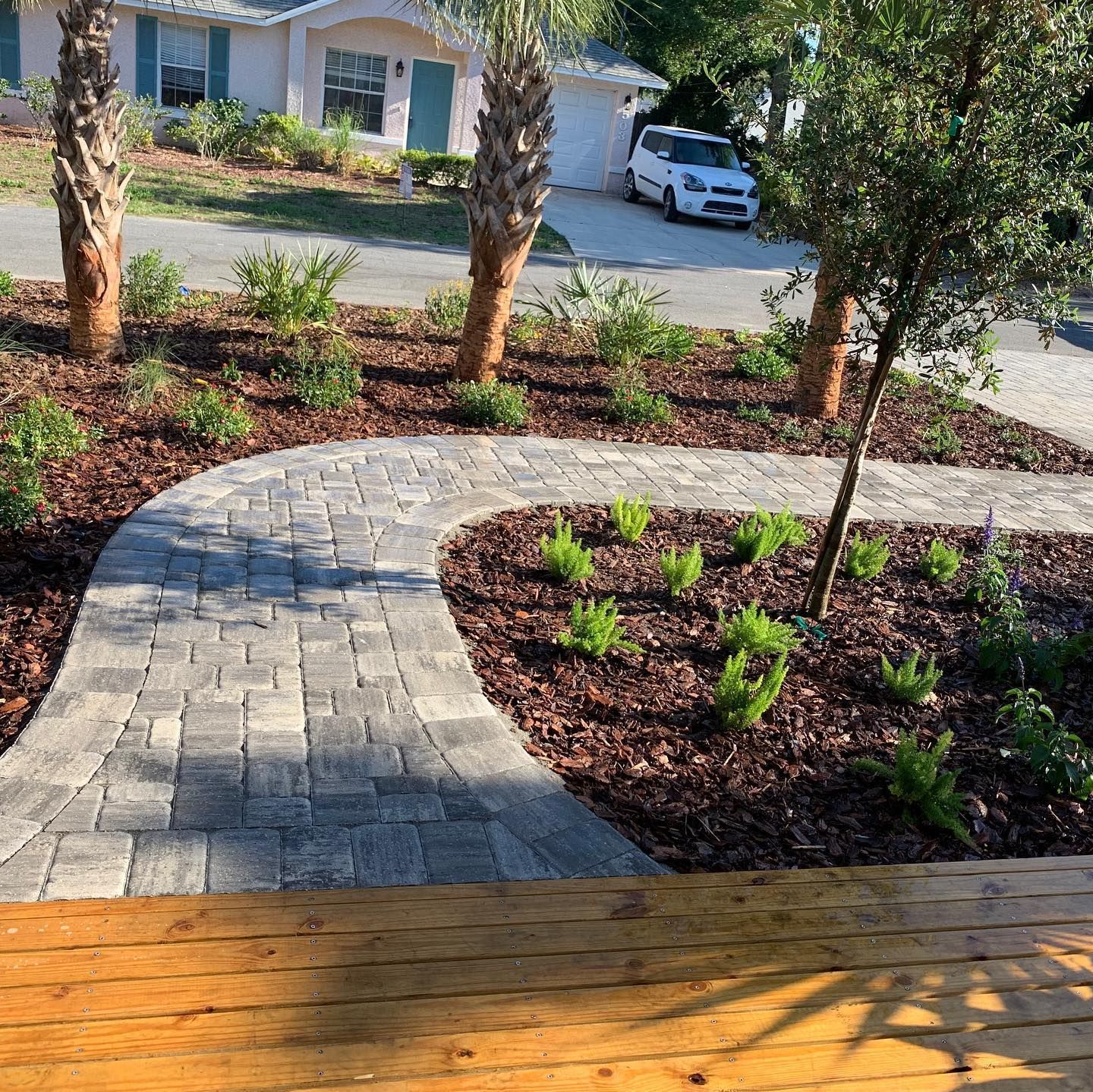 A brick pavement leading to a house with a car parked in the driveway.