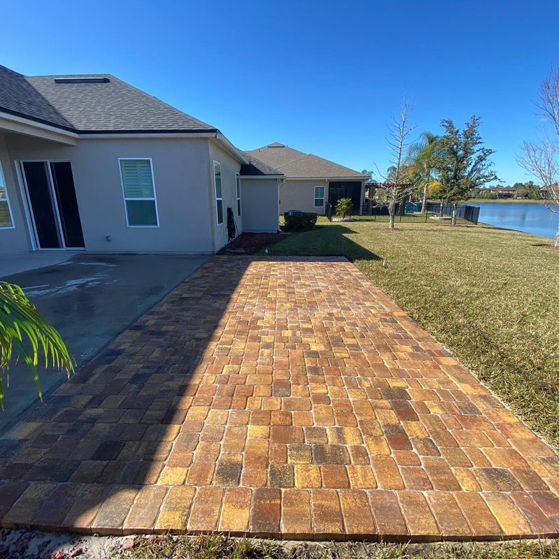 A brick pavement leading to a house with a lake in the background