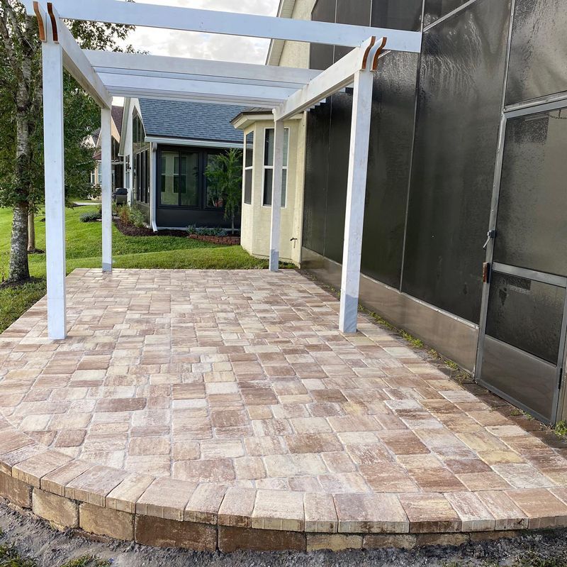 A brick patio with a white pergola in front of a house