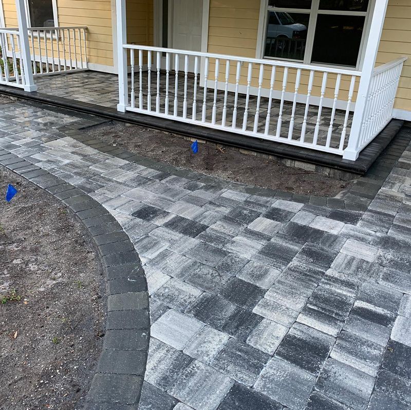 A brick walkway leading to a porch of a house.