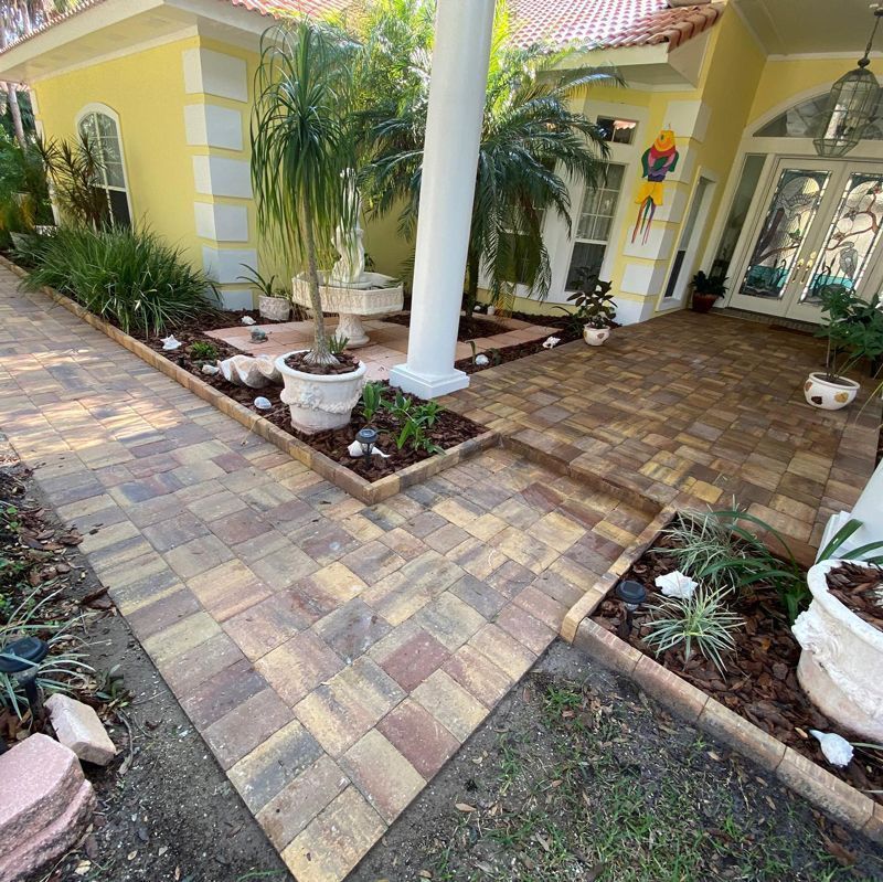 A brick walkway leading to a yellow house with potted plants.