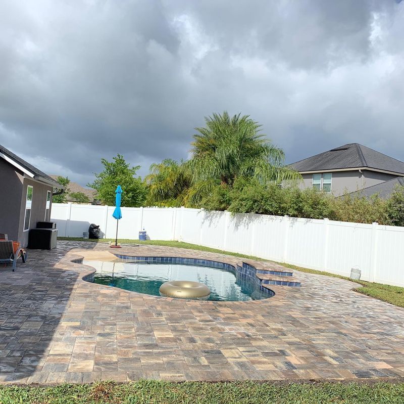 A backyard with a swimming pool and a white fence