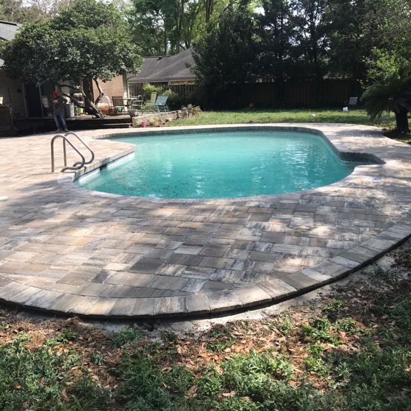 A large swimming pool is surrounded by a brick patio.