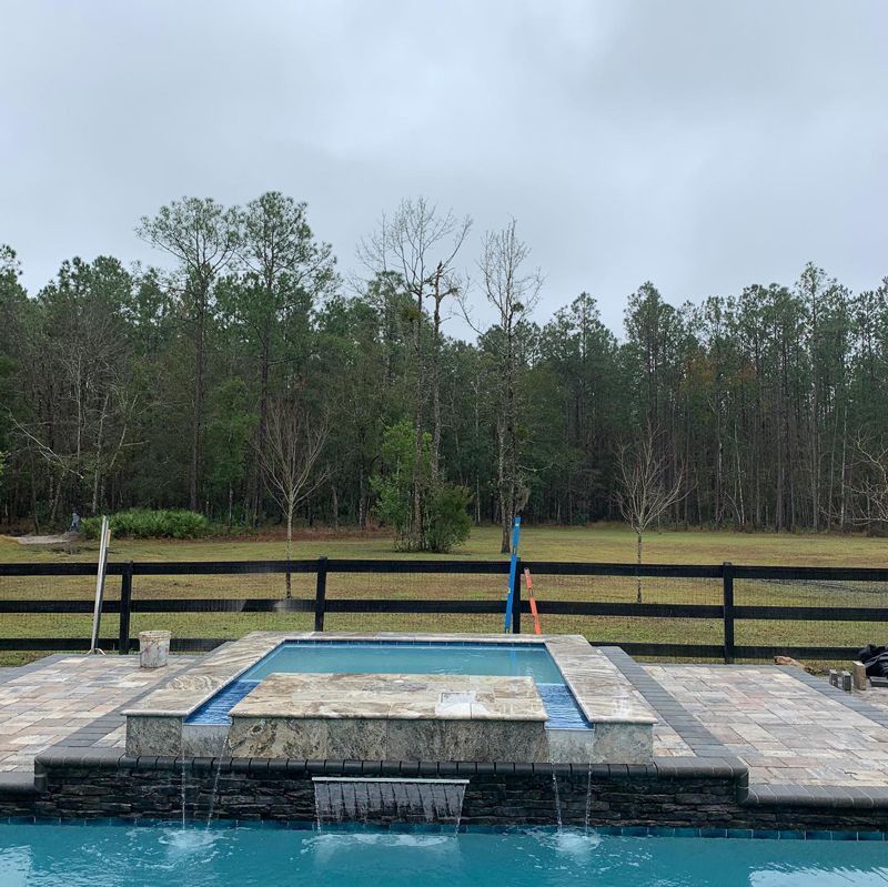 A swimming pool with a waterfall and a fence in the background.