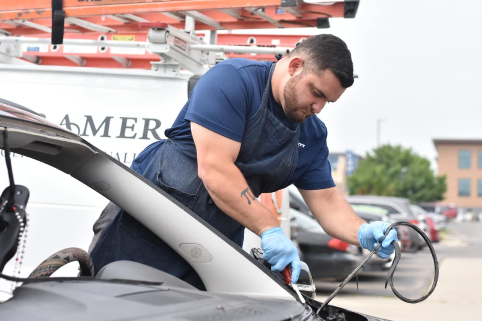 Auto glass technician in blue shirt and gloves repairing a car windshield.