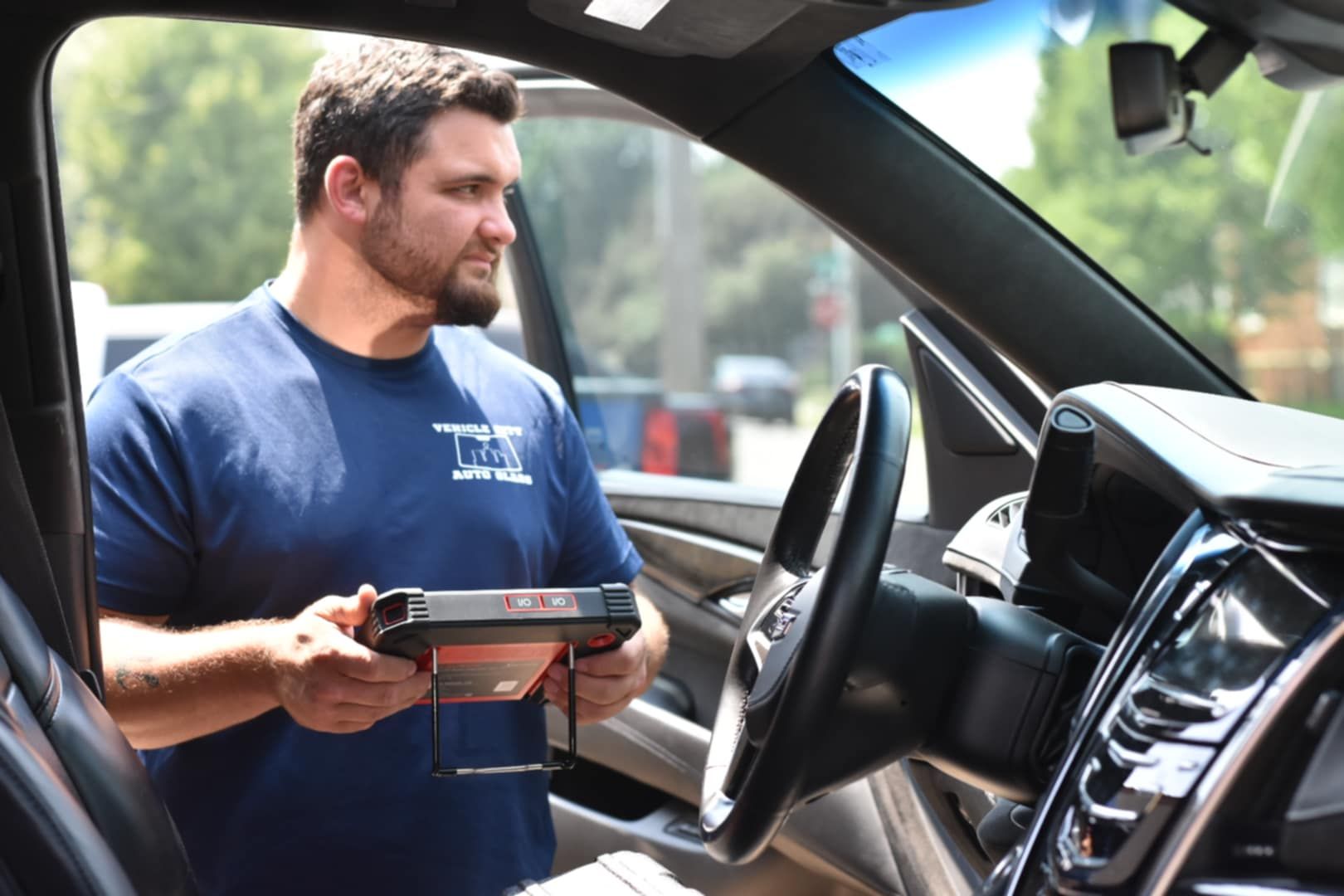 Mechanic using diagnostic tool inside a car; outdoors.