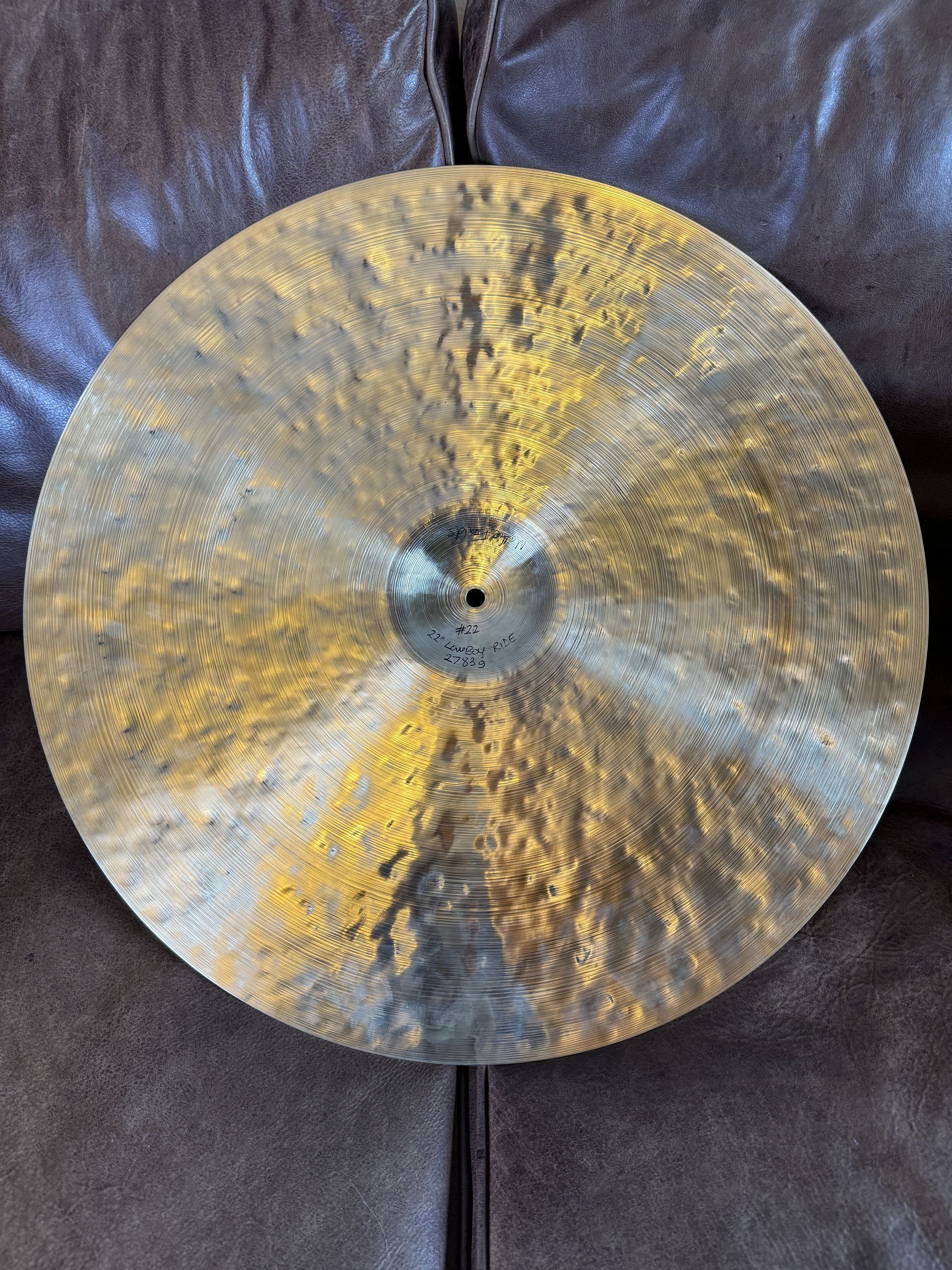 Bronze cymbal, circular with a central hole, resting on a brown leather couch.